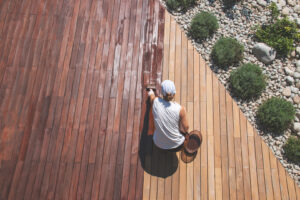 A woman exterior painting the wooden floor of an outdoor deck.