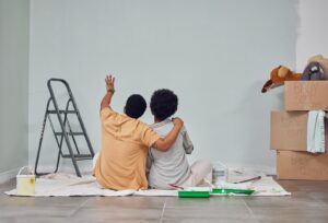 A young couple, backs to the audience, admiring the freshly painted wall. The couple has just finished their DIY project after carefully valuing interior painting cost.