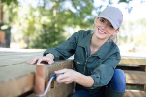 A woman painting a deck, focusing on covering all wooden planks evenly. The scene highlights her methodical approach to deck staining.