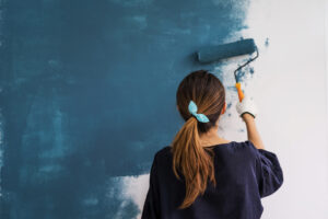 A woman is painting a wall vibrant blue. She is carefully applying the paint with a roller after considering interior painting cost.