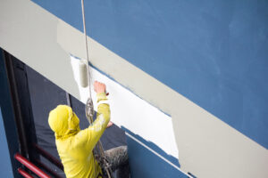 A commercial painter is commercial painting an exterior wall of a building, using a roller to apply a fresh coat of paint.