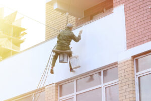 A man is painting the outside of a balcony, focusing on exterior house painting.