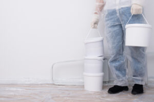 A selection of paint containers and cans are seen on the floor, with the legs of a worker visible in the background. The image highlights the equipment used by Wichita professional painters.