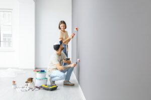 A happy couple painting their walls, demonstrating how to paint over wallpaper for a refreshed appearance.