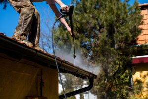 A person using a pressure washer to clean a rooftop, demonstrating the effectiveness of pressure washing.