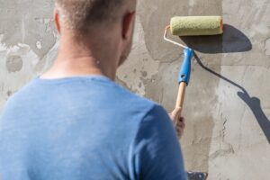 A man is painting an external wall with a roller, demonstrating the process of exterior house painting.