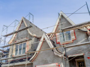 A scaffolded exterior of a house with an exterior house painter working on the walls.