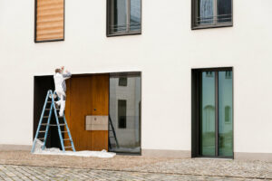 A man on a ladder painting the exterior of a commercial building, showcasing the work of a professional commercial painter.