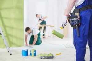 A man with a roller is standing in front of his team, who are also painting a large exterior wall. This image highlights the variety of painting services Koehn Painting offers.