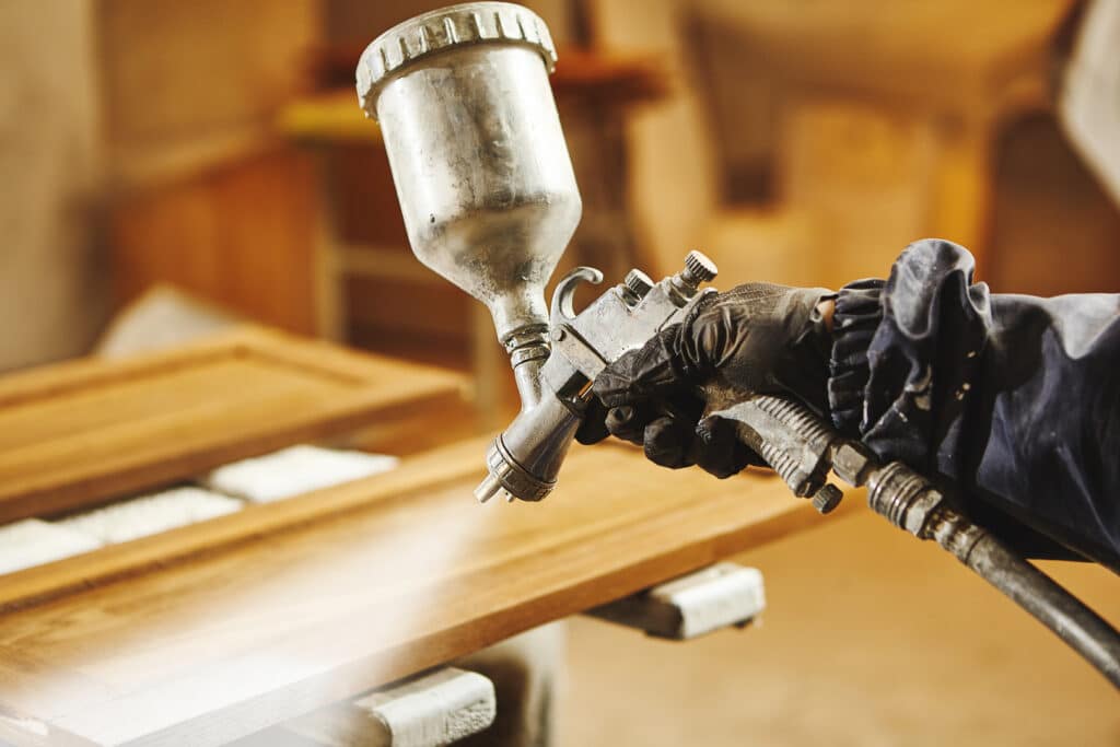 A professional using a spray gun to paint kitchen cabinets, emphasizing the expertise of a dedicated cabinet painter.