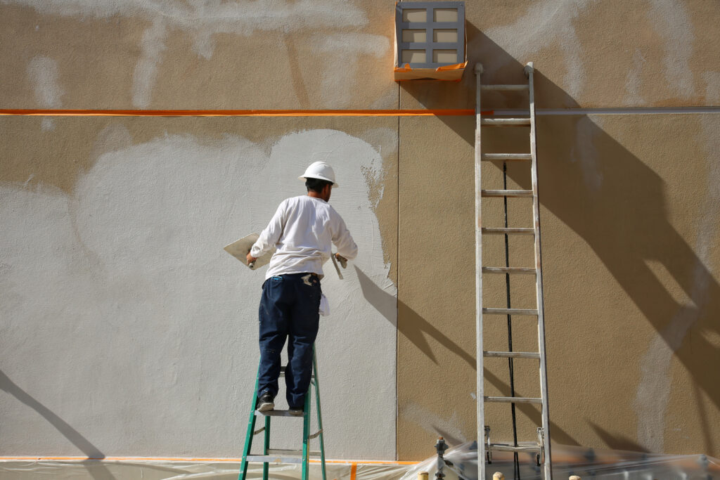 House painters in Wichita, KS, diligently painting an exterior wall, ensuring a smooth and professional finish.