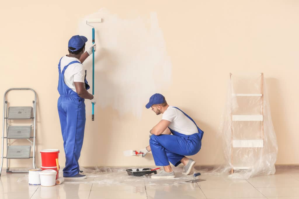  house painter painting a wall, working together with brushes and rollers to apply a fresh coat of paint.