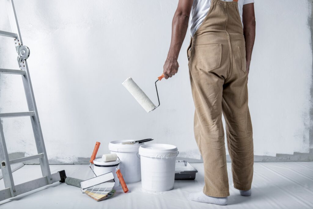 An exterior house painter using a roller to apply paint evenly on a large wall, ensuring a smooth finish.