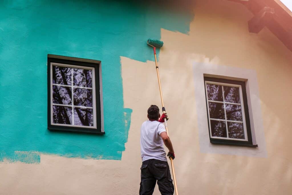 An external painter from a reputable home painting service is painting the side of a house.