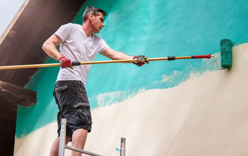 Exterior house painting contractors carefully painting a house wall with a roller, ensuring an even coat.