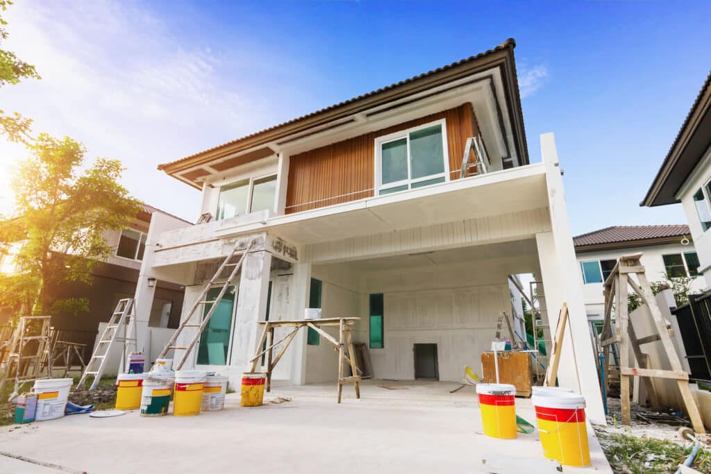 A home being painted by a exterior painting companies, with several buckets of paint and other supplies scattered around.