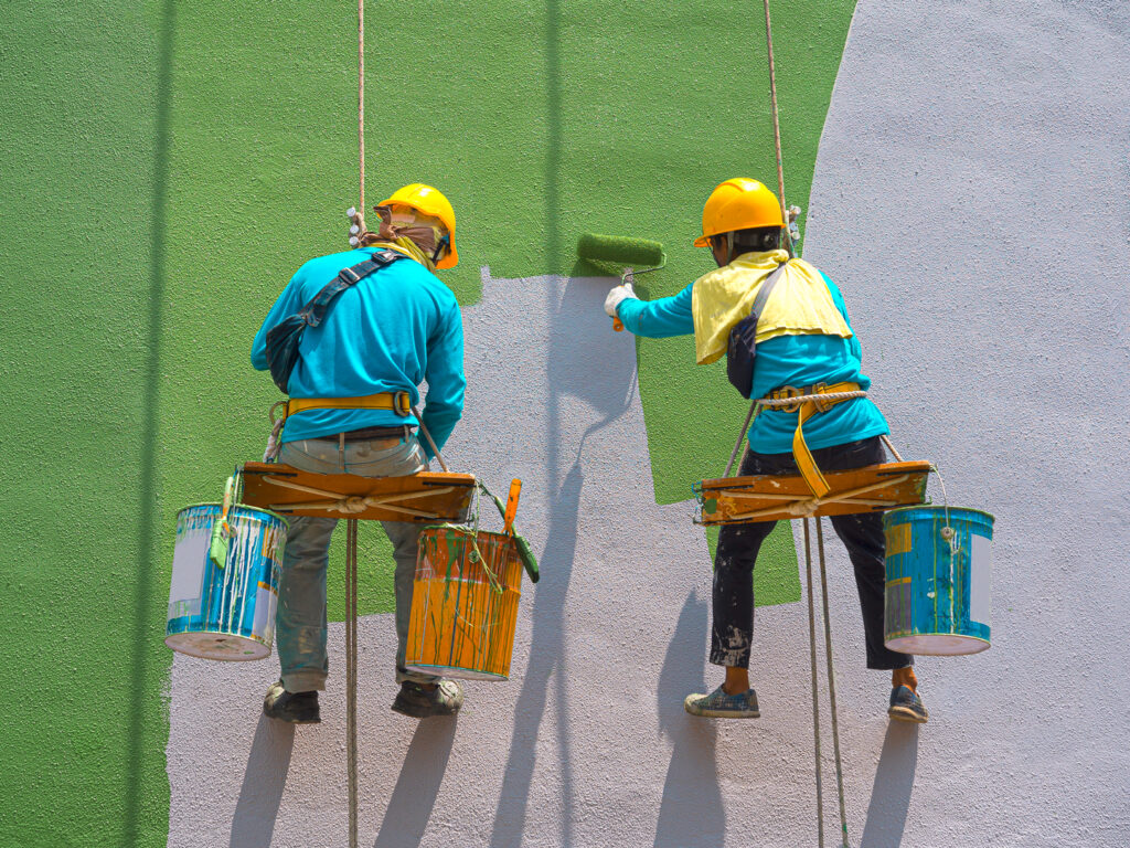 Two painters painting an external wall green, highlighting the skills of exterior house painters.