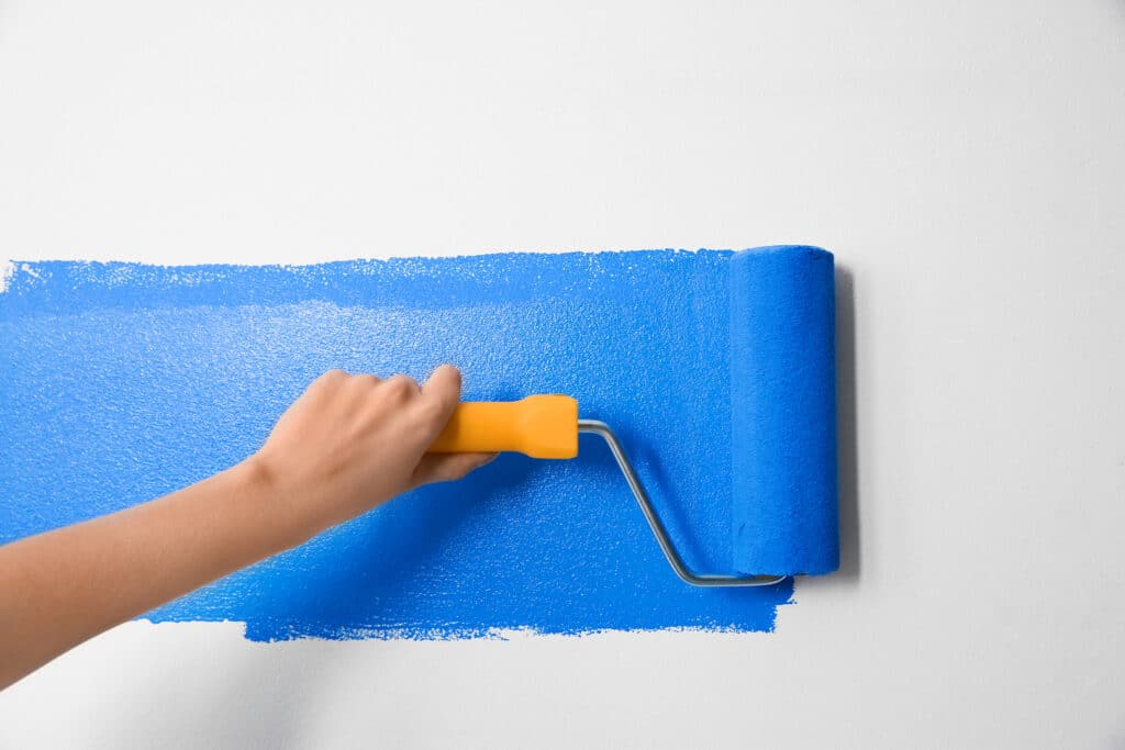 A hand using a roller to apply blue paint on a wall, reflecting the meticulous attention to detail offered by Wichita painting professionals.