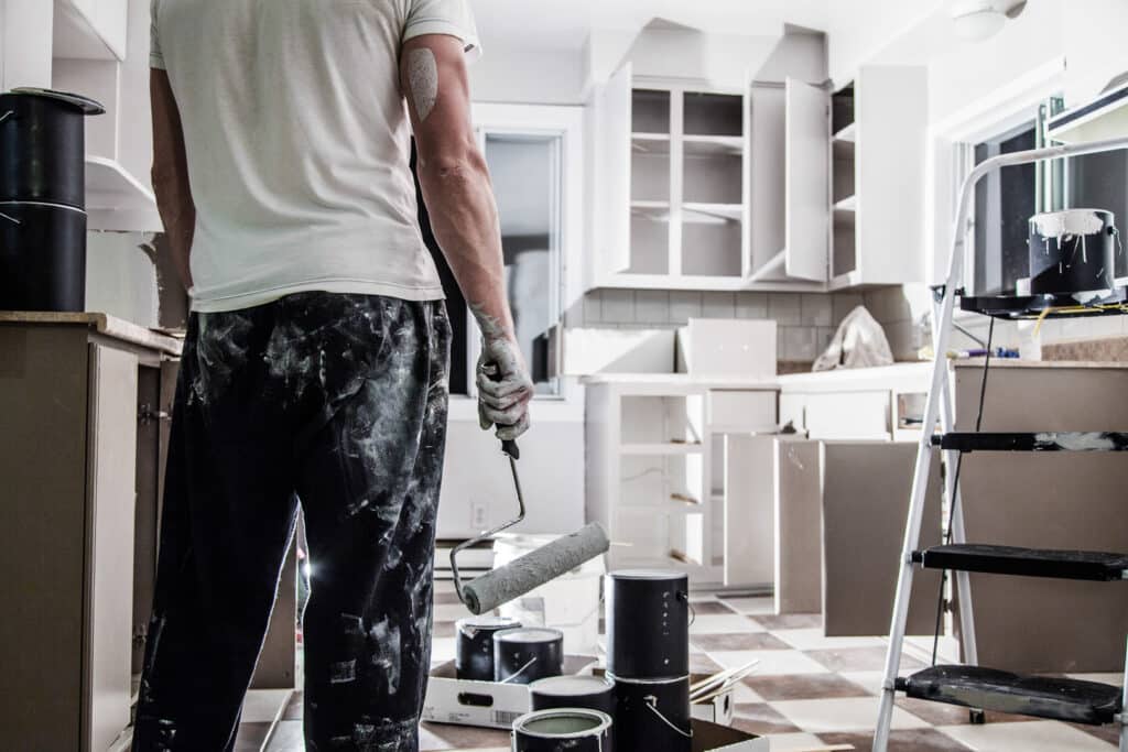 A painter with a roller standing in front of a kitchen, ready to provide kitchen painting services.