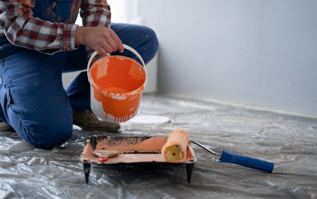 A contractor pouring paint into a roller tray, preparing for a detailed painting task inside a room for his painting contractors.