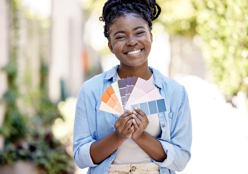 A smiling woman holds up a fan of paint swatches, representing various color options for projects for paint contractors.