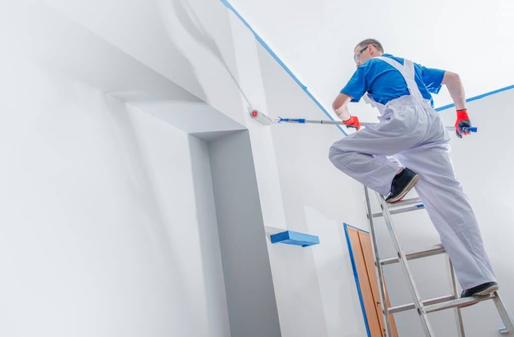 A professional painter standing on a ladder while applying a fresh coat of paint on a wall, demonstrating the effectiveness of professional painting solutions.