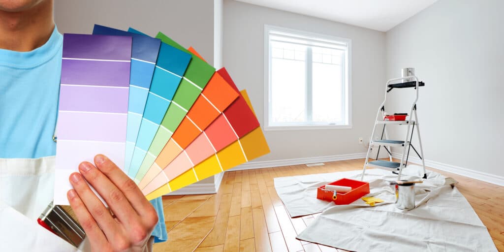 A person holding various paint color swatches in a room prepared for painting, indicating the choices provided by a professional painting service.