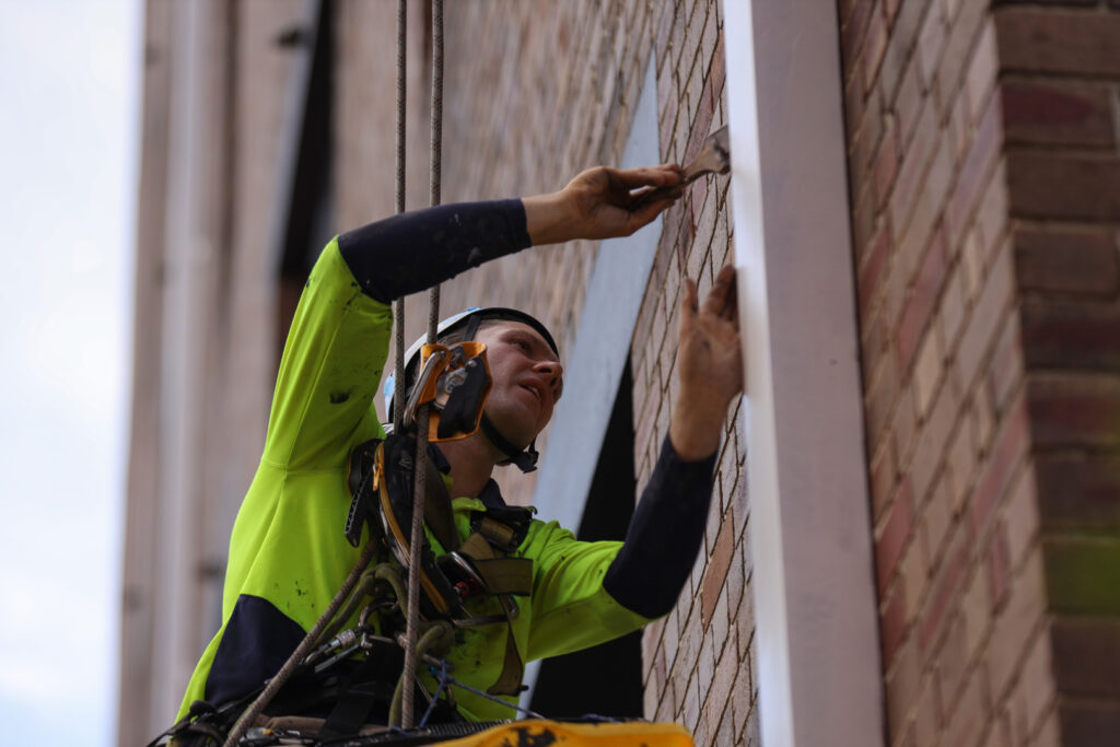 A worker carefully painting a commercial building’s exterior.