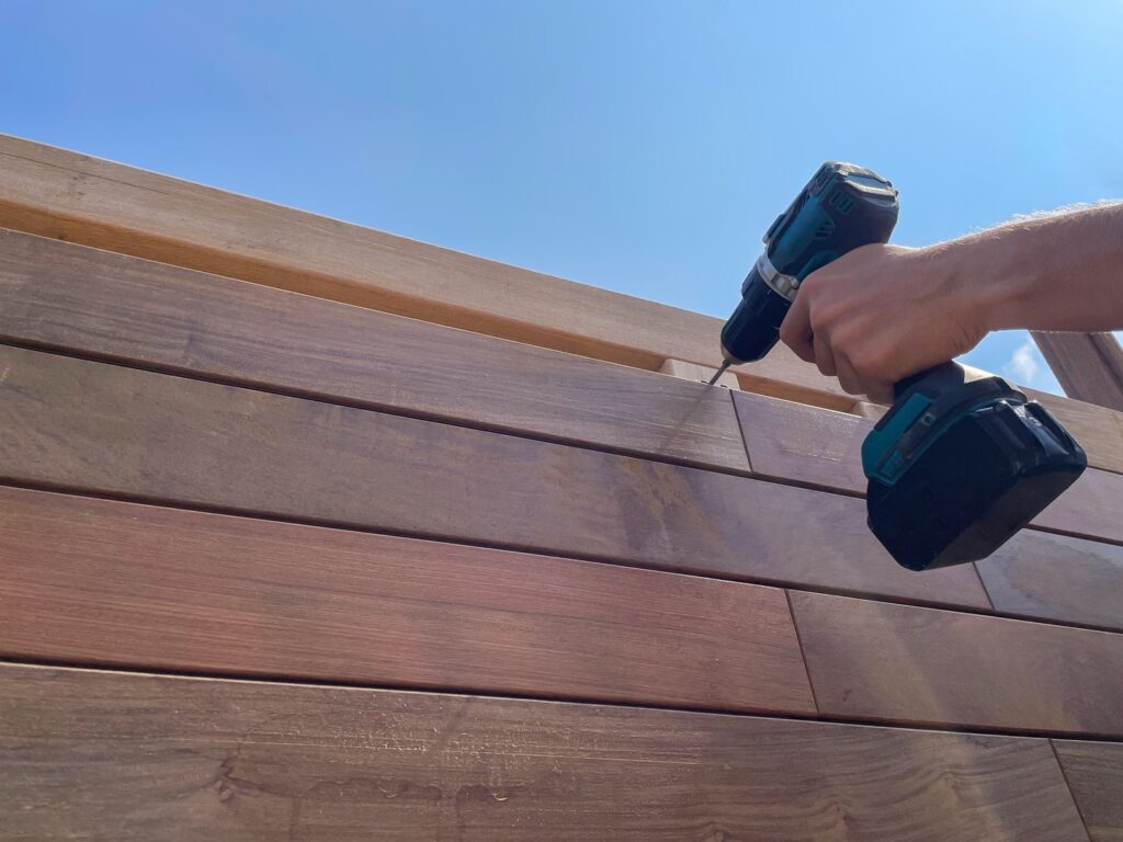 A person using a drill to fix siding damage on a residential property. This image showcases the repair process of wooden siding using power tools. Fixing siding damage early helps prevent further structural issues.