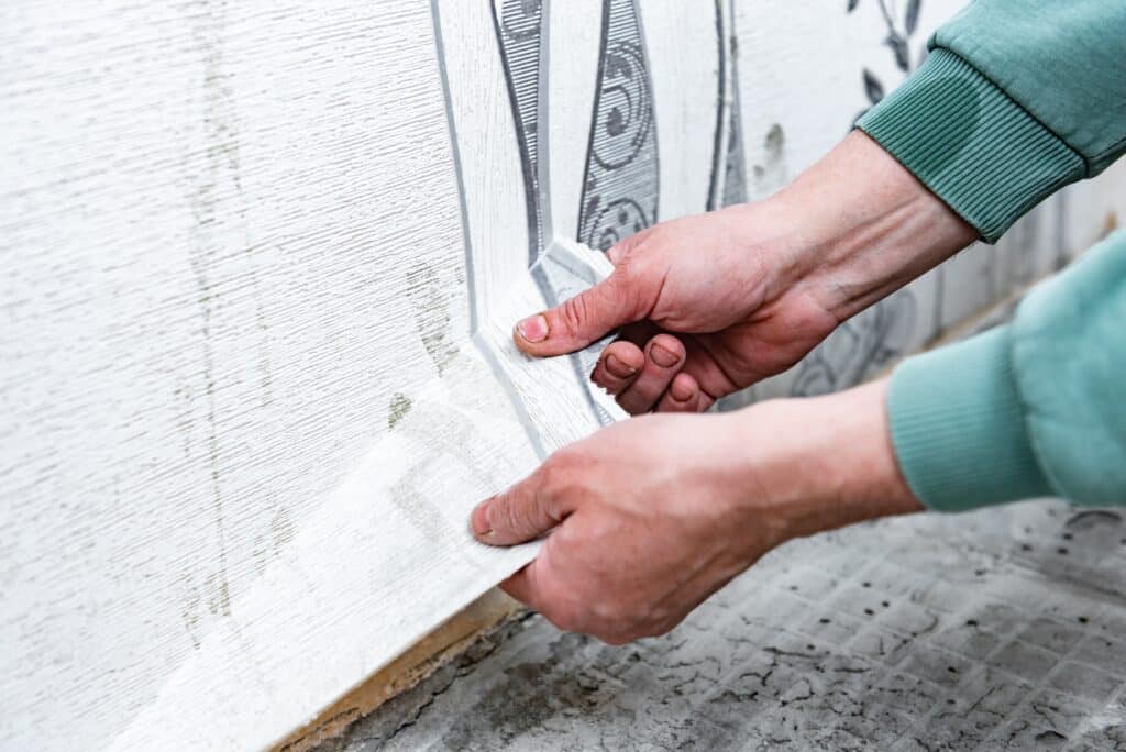 Hands smoothing out wallpaper, illustrating the technique required to paint over wallpaper smoothly and evenly.