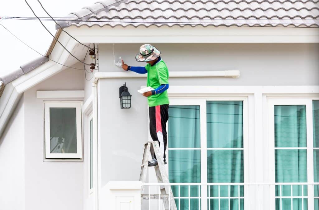 House painters in Wichita carefully applying paint to the exterior of a home while standing on a ladder.