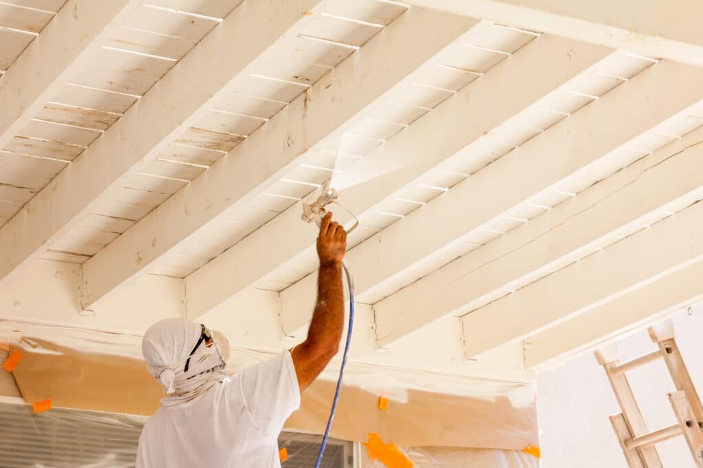 A painter in Wichita spray painting wooden beams, showcasing professional work by painting contractors in Wichita.