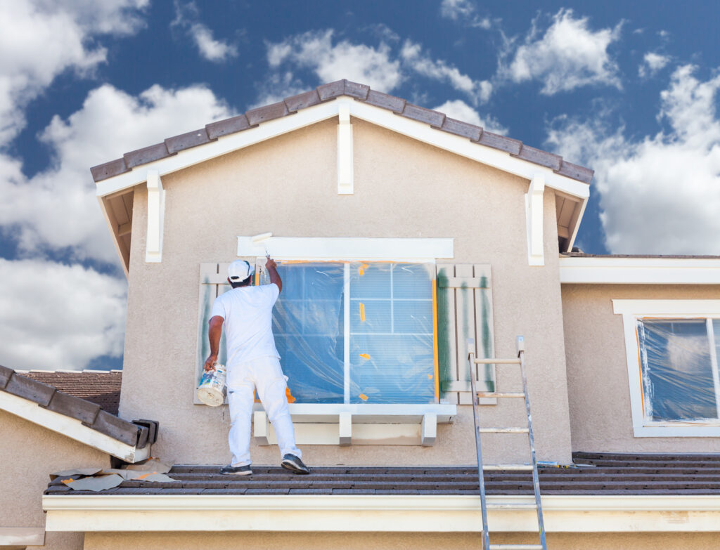 A painter is applying white paint to the exterior of a home, as part of exterior painting in Wichita KS .