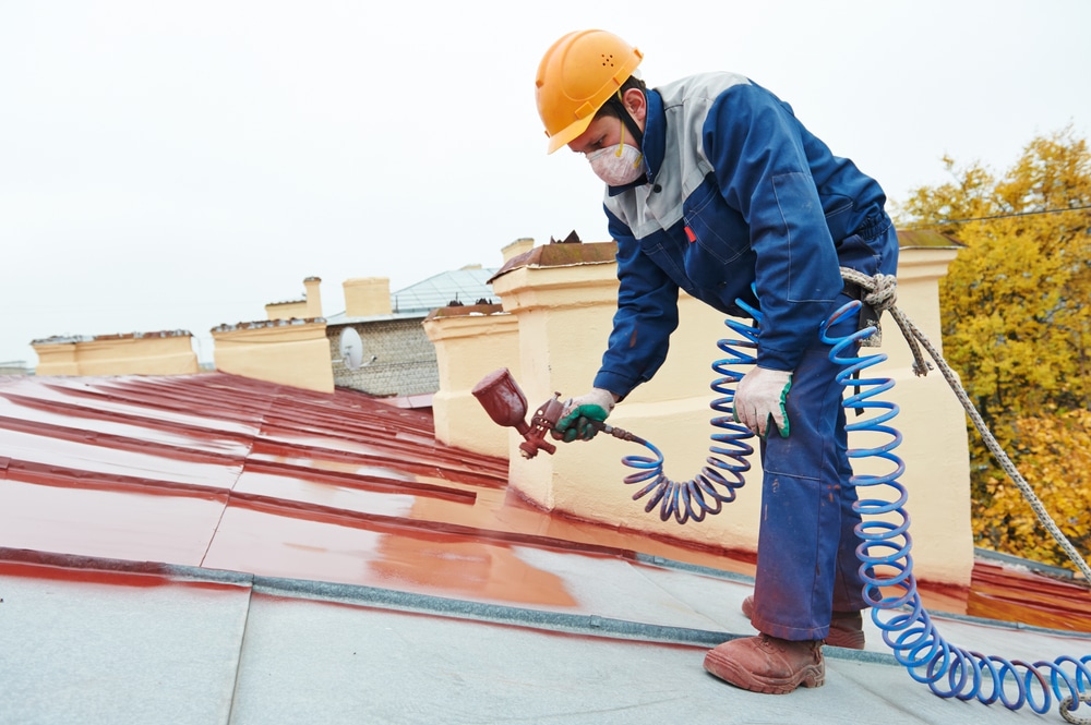 A painter with commercial painting certification wearing protective gear, while painting a roof.