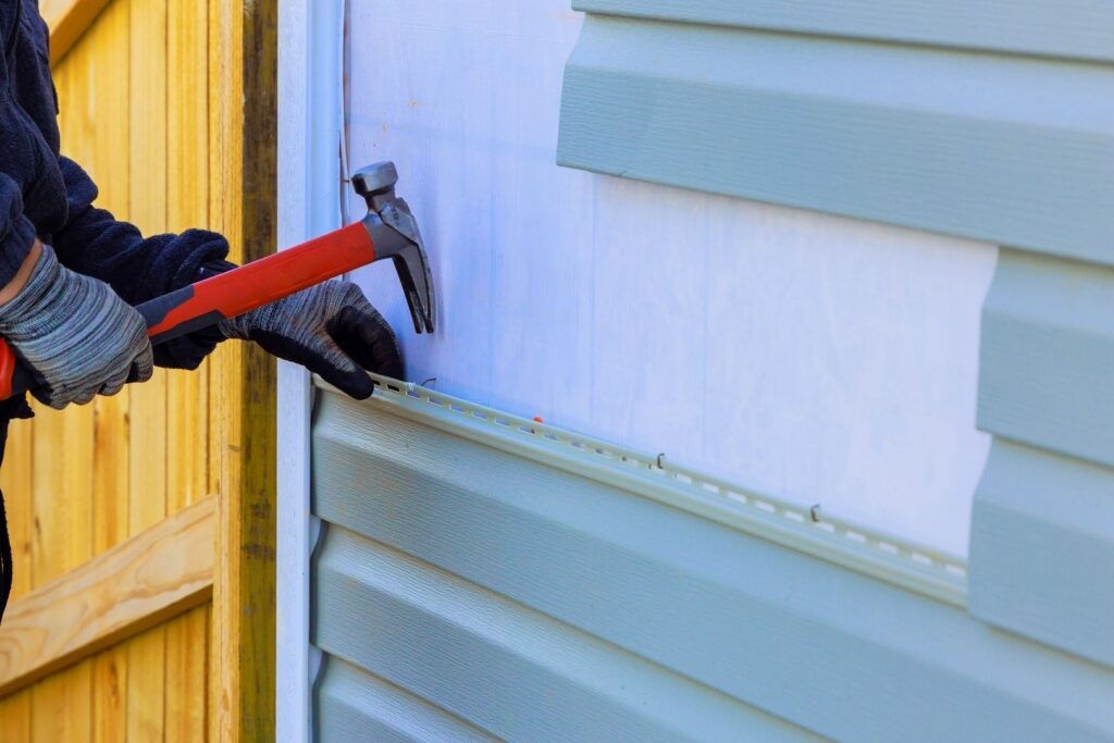 Worker hammering vinyl panels, showcasing the precision of a trusted siding contractor.