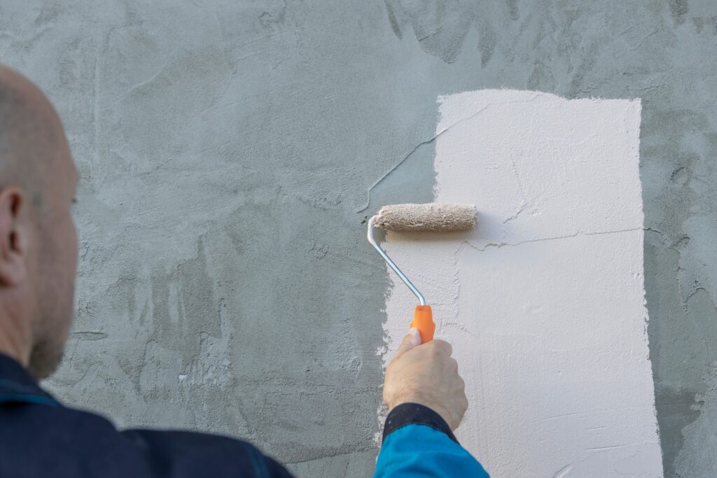 A painter rolling a light-colored paint over a concrete wall, showcasing the work of Wichita KS painters.