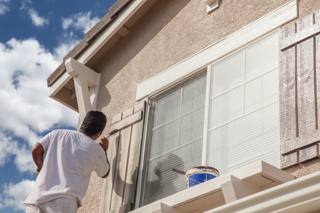 A painter carefully applying paint to exterior window trim, completing a residential painting project.