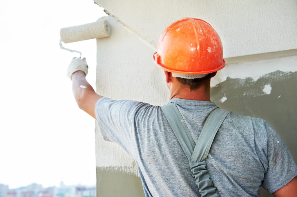 An OSHA-compliant painter wearing a hard hat and protective gear while painting a wall.