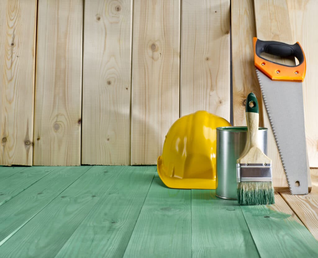 Tools and equipment used by a professional painter, including eco-friendly paint, a brush, and safety gear, set against a natural wood backdrop.