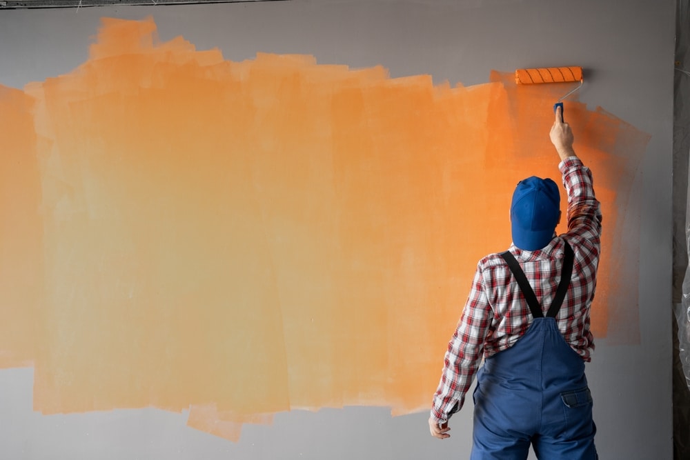 Worker applying vibrant orange paint to a business interior wall with a roller, showcasing professional interior painting services.