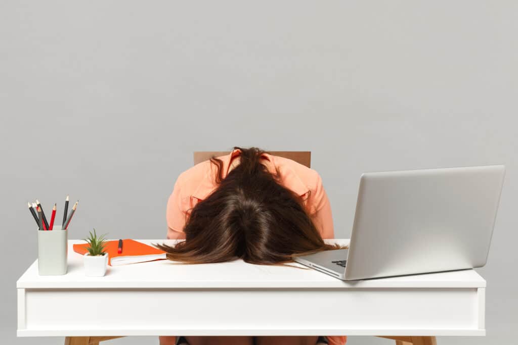 Frustrated woman with her head on a desk, surrounded by one of the worst colors for an office space: gray.