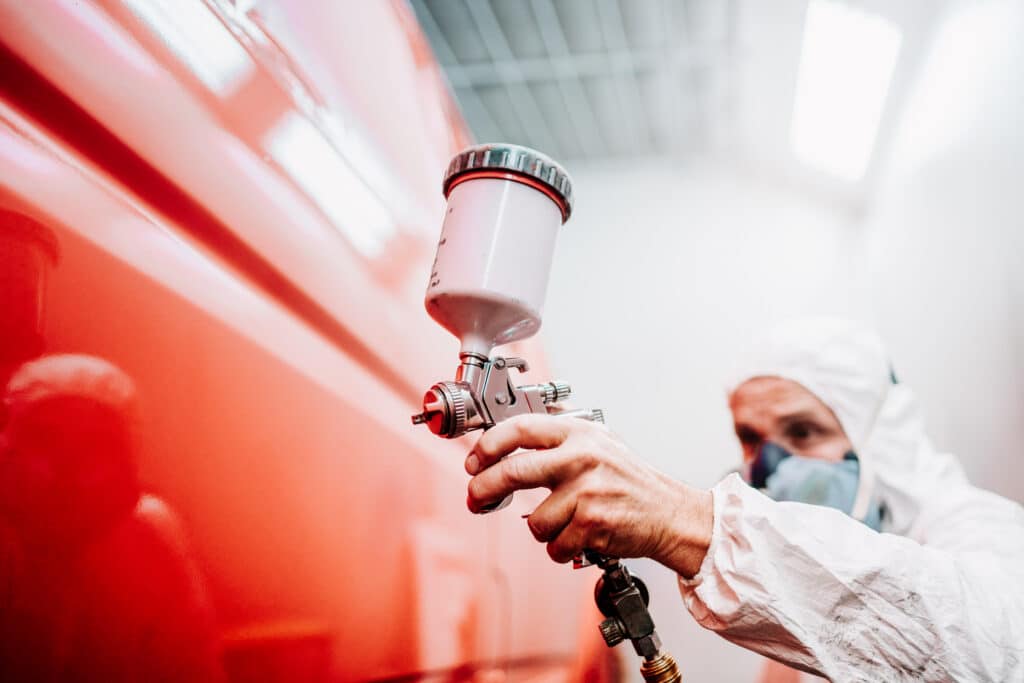 Professional painter using a spray gun to apply red paint in a controlled environment, highlighting precision and expertise in the painting industry