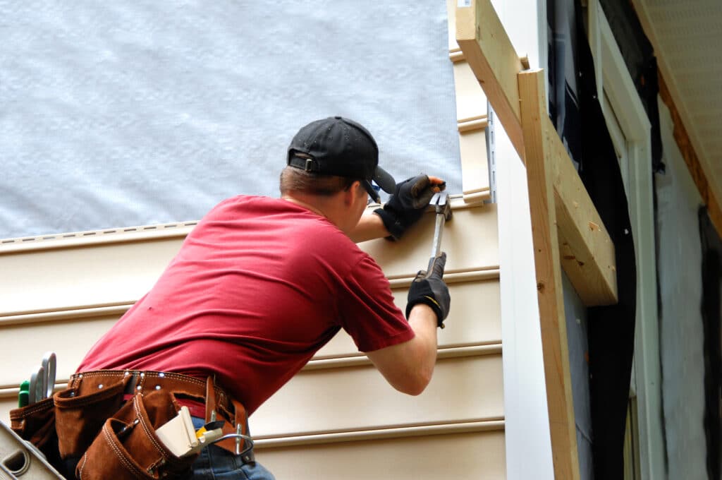 A professional technician performing siding repairs, using specialized tools to securely install panels, showcasing the expertise and precision needed for high-quality results.