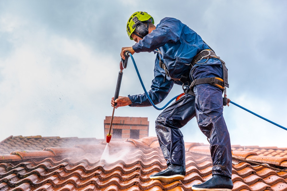 A professional man dressed in working clothes cleaning a roof with a commercial power washing machine.