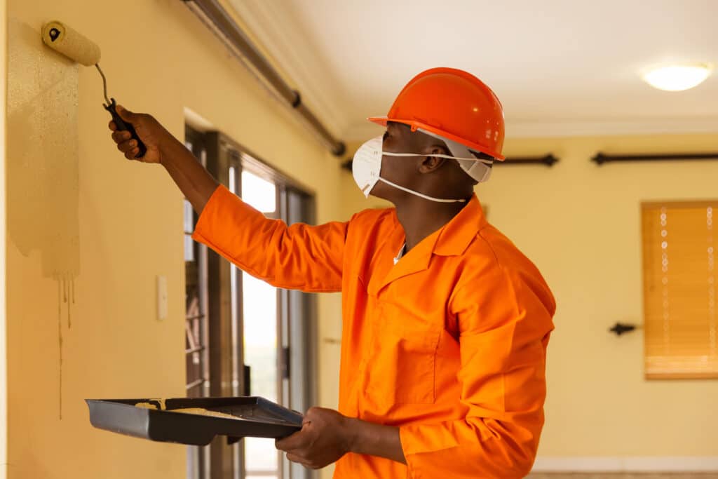 Painter wearing protective gear to prevent paint allergy, showcasing safety measures while applying paint indoors.