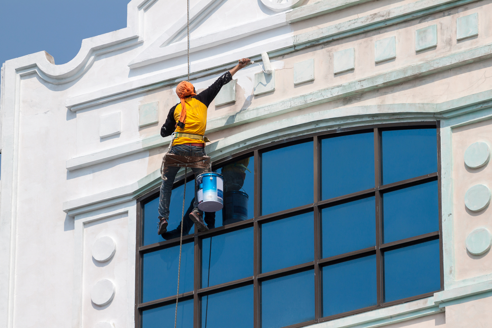 Skilled commercial painting contractors suspended by ropes, carefully applying a fresh coat to a building's exterior.