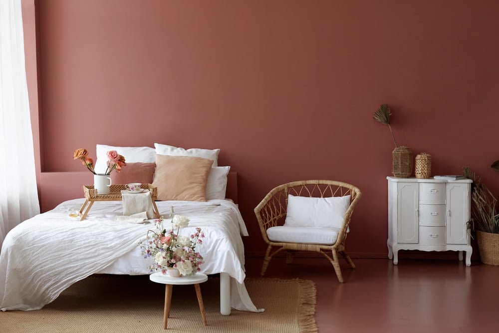 Stylish modern bedroom with freshly painted terracotta walls, contrasting a space where interior paint is aging out to emphasize the benefits of timely repainting.