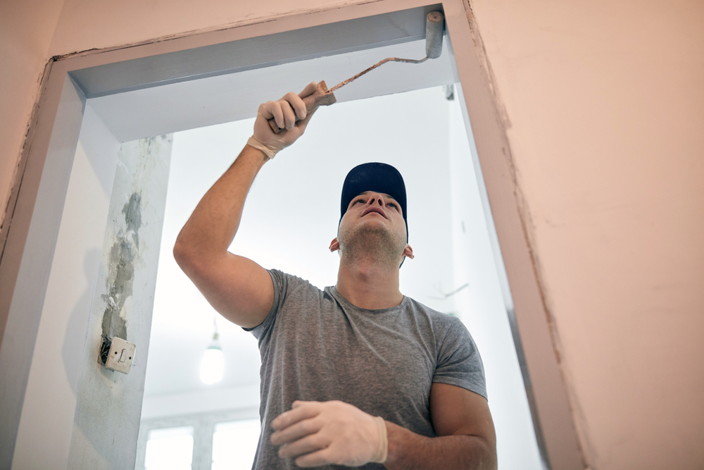 Man painting the top frame of a doorway during a home remodel, symbolizing hands-on labor and cost-effective upgrades, illustrating 'what is the 30% rule for home renovation,' where no more than 30% of a home's value is spent on improvements to avoid overcapitalization.