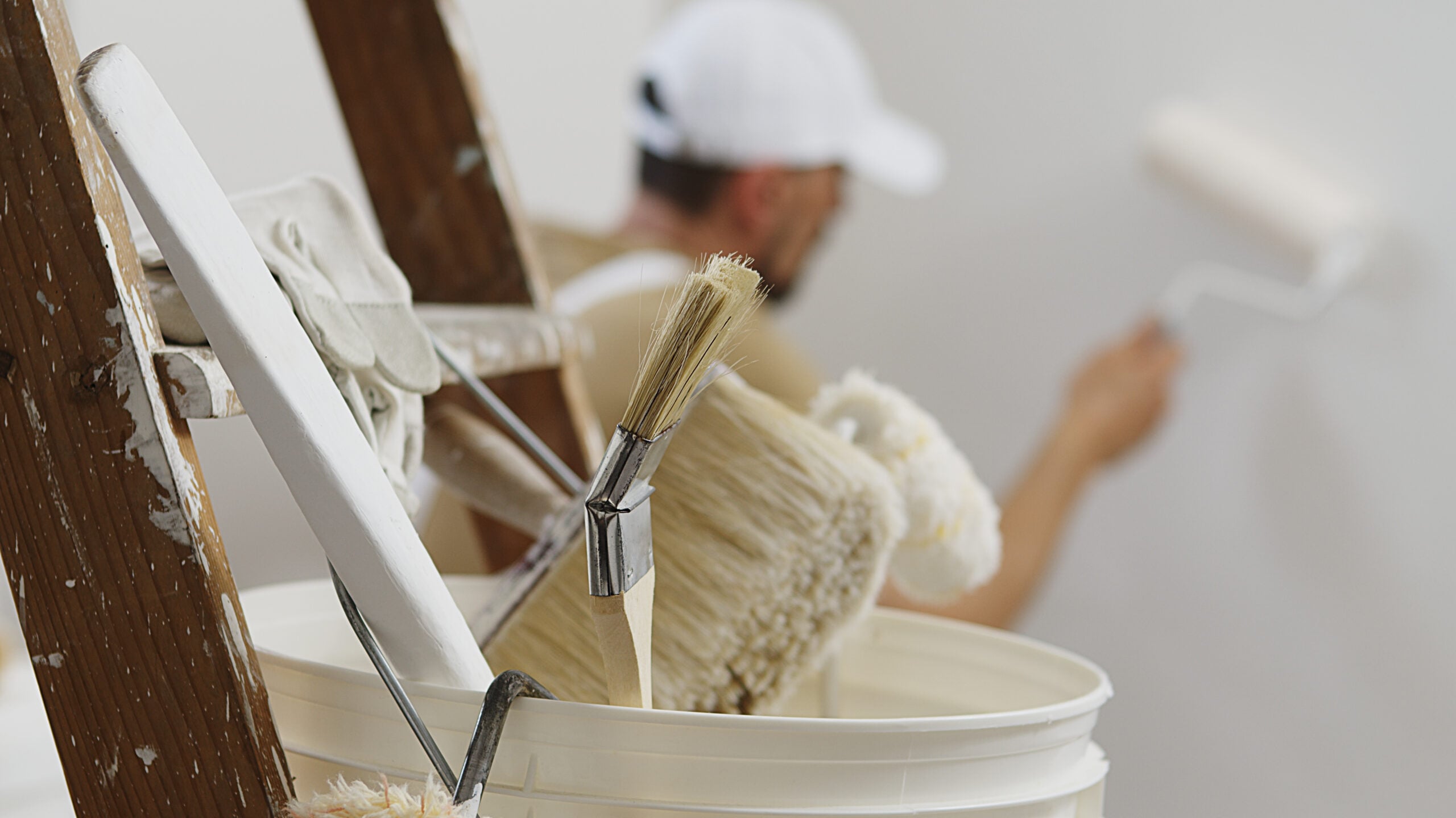 A close-up of painting tools, including brushes and rollers, with a professional painter in the background, showcasing the precision and quality of professional painting services.