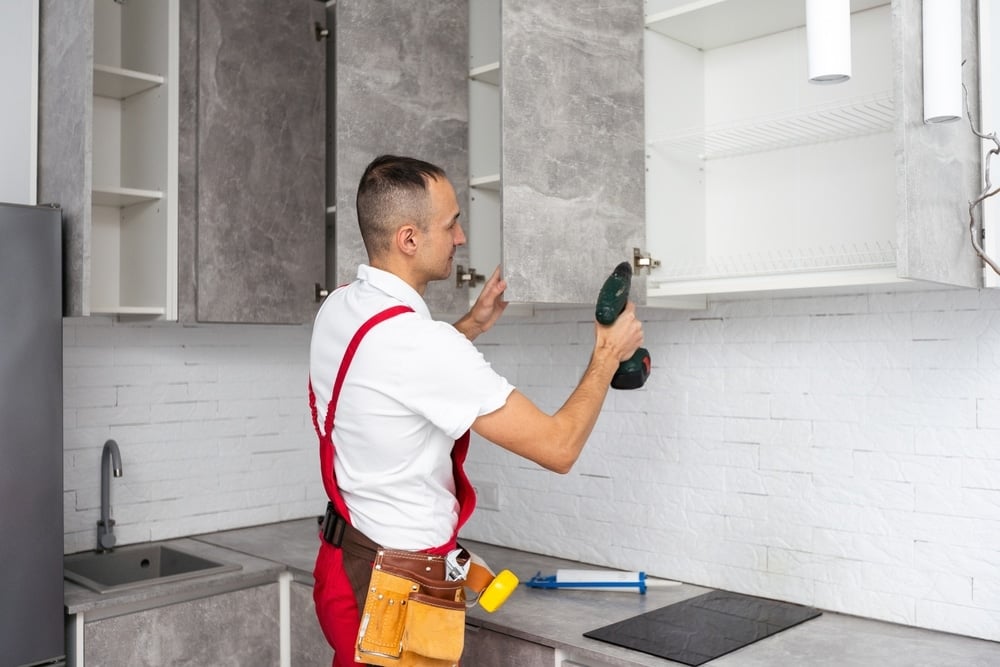  Worker installing kitchen cabinets with a drill showing renovation work and reflecting how kitchens often deliver a high rate of return on home improvements.